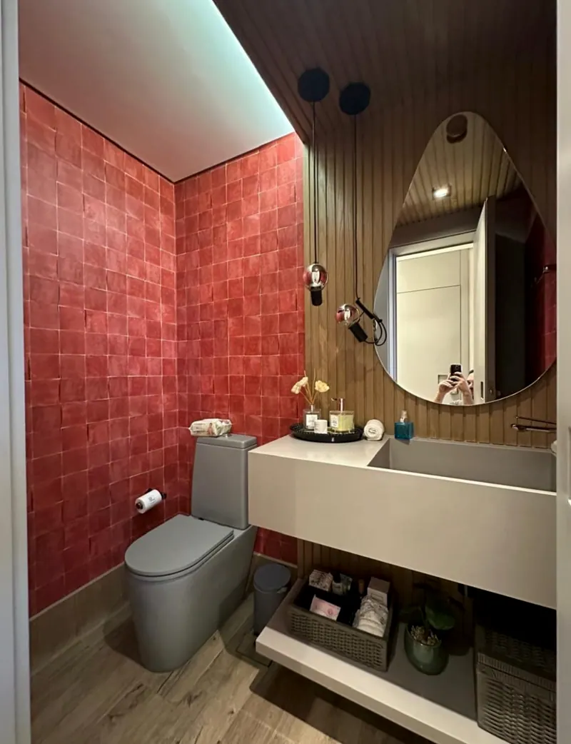 Lavabo com parede de revestimento vermelho, painel de madeira, espelho oval e bancada branca