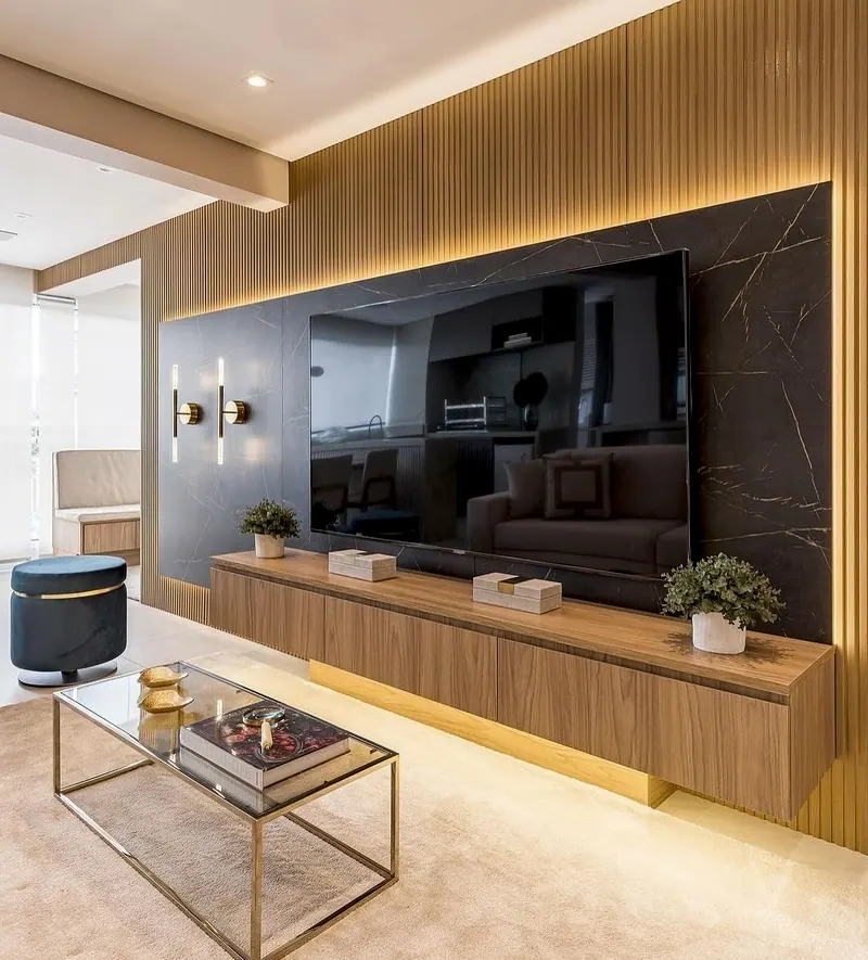 Sala com painel de pedra preta com veios dourados, TV e rack de madeira com luz embaixo