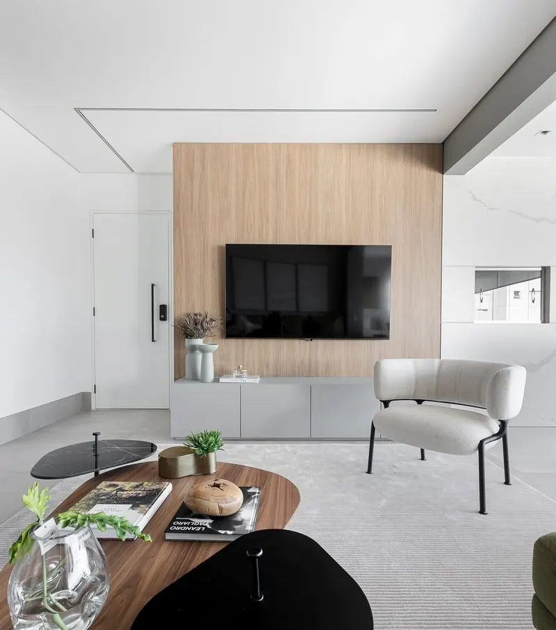 Sala clara com painel de madeira, TV, poltrona e mesa de centro