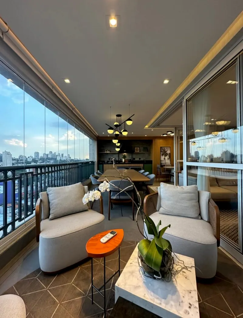 Varanda envidraçada com poltronas, mesa de centro e a sala de jantar ao fundo